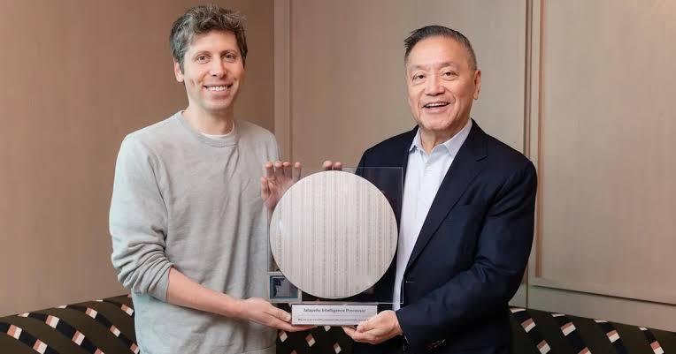 Senior technology executives Sam Altman and Hock Tan stand side-by-side in an office setting, holding a circular, reflective 300mm silicon wafer containing custom-designed OpenAI Jalapeño inference chips.