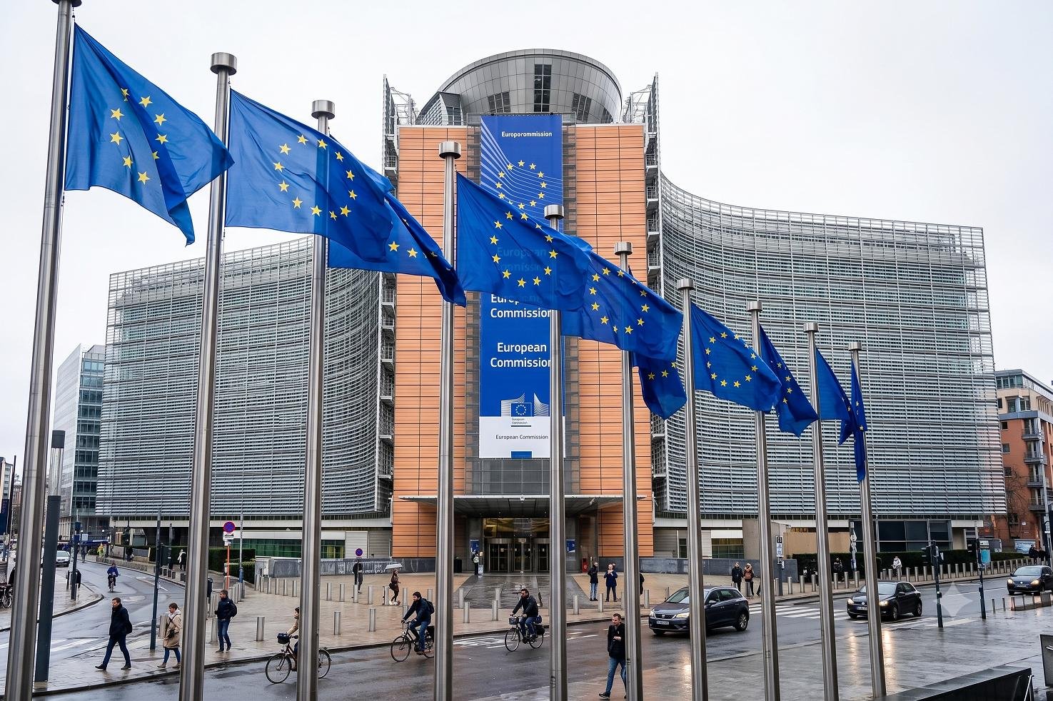 The European Commission headquarters building in Brussels, showing EU flags against a clear sky.